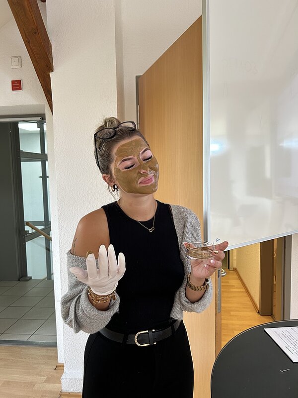 Eine Auszubildende zur Erzieherin posiert, mit Heilerde im Gesicht, lächelnd für ein Foto.