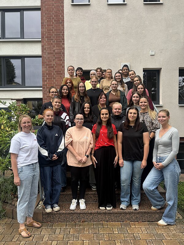Große Gruppe von Schüler*innen und Mitarbeitenden der Euro Akademie Zwickau steht für ein gemeinsames Gruppenfoto auf einer Außentreppe vor dem Schulgebäude.