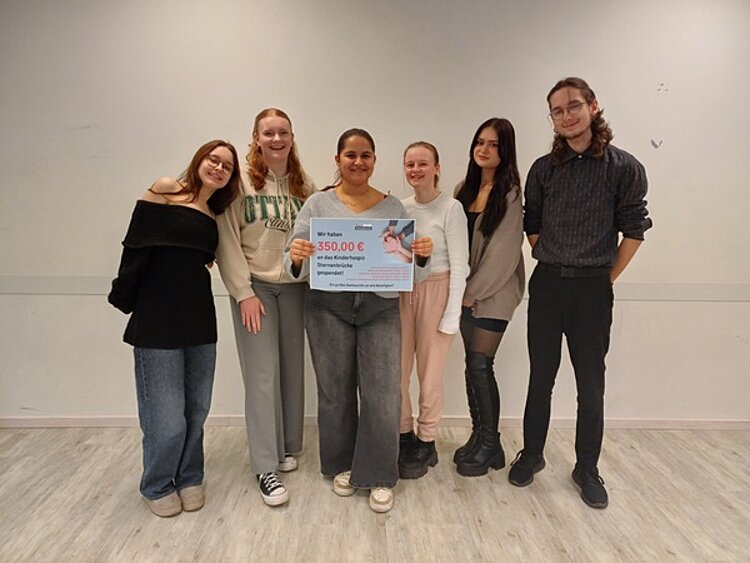 Spende an das Kinderhospiz Sternenbrücke Sechs lächelnde Schüler und Schülerinnen posieren mit mit Spendenscheck für ein Gruppenfoto.