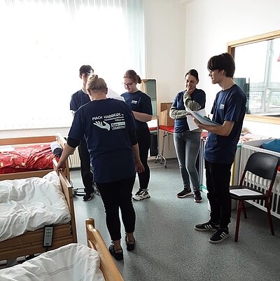 In einem Raum mit drei Krankenbetten führen die Auszubildenden eine praktische Übung durch. 
