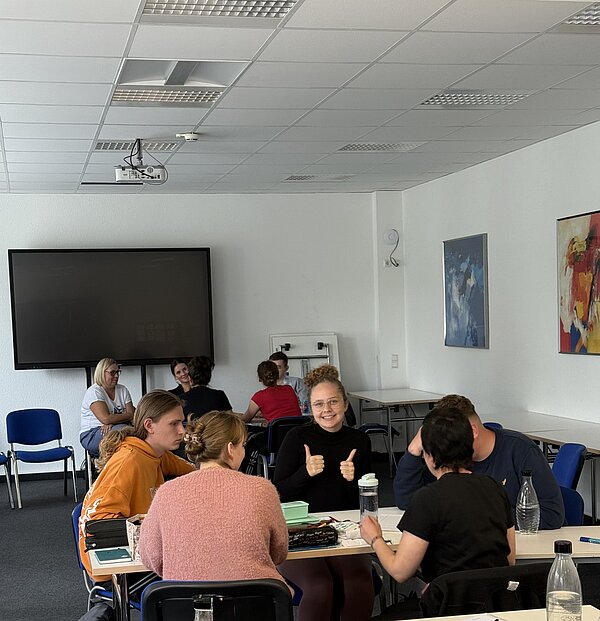 Foto von einer Gruppe von Schülern, auf dem eine lächelnde Schülerin beide Daumen nach oben hält