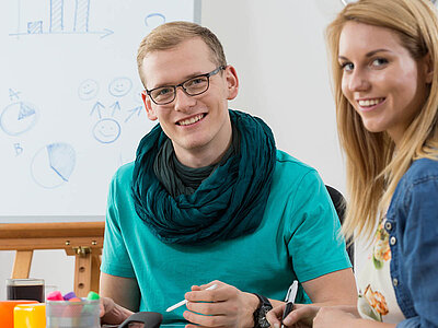 Zwei Personen arbeiten zusammen an einem Whiteboard mit einfachen Zeichnungen und Diagrammen.