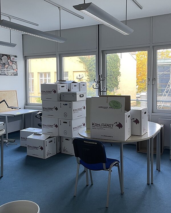 In einem Raum, der mit blauem Teppich ausgelegt ist, stehen Tische, auf denen wiederum zahlreiche Kartons stehen. 