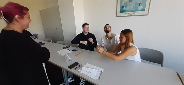 „Die Neuen“ sind da – Euro Akademie Mainz begrüßt neue Klasse der Fremdsprachenkorrespondenten Drei Personen arbeiten an einer Marshmallow-Challenge, eine Person hält das Marshmallow oben, während die anderen zusehen und lachen.