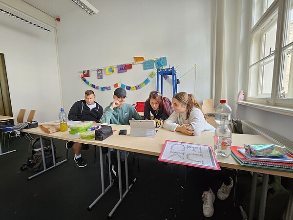 Podcast-Projekt: KAFFEE TRINKEN & SPIELEN Schülerinnen und Schüler der Euro Akademie Halle sitzen an Tischreihen und besprechen sich.