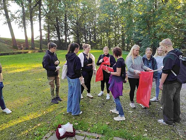 Schülerinnen und Schüler auf einer Wiese beim Aufräumen mit Mülltüten und Zangen in den Händen.