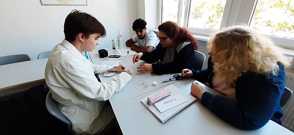 „Die Neuen“ sind da – Euro Akademie Mainz begrüßt neue Klasse der Fremdsprachenkorrespondenten Vier Personen sitzen an einem Tisch im Klassenzimmer und arbeiten gemeinsam an einer Übung mit Fäden, Stäbchen und Marshmallows.