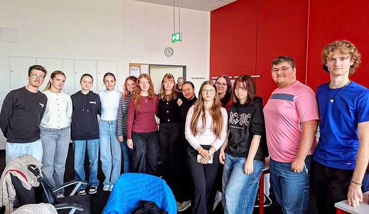 Schülerinnen und Schüler aus der Slowakei posieren an der Euro Akademie Bamberg für ein Gruppenbild. Alle sind leger gekleidet in sportlichen Pullovern, ein Schüler in einem rosa T-Shirt, ein anderer in blauem T-Shirt, im Hintergrund sieht man eine dunkelrot gestrichene Wand. Alle lächeln gut gelaunt in die Kamera. 