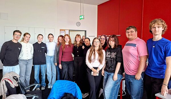 Schülerinnen und Schüler aus der Slowakei posieren an der Euro Akademie Bamberg für ein Gruppenbild. Alle sind leger gekleidet in sportlichen Pullovern, ein Schüler in einem rosa T-Shirt, ein anderer in blauem T-Shirt, im Hintergrund sieht man eine dunkelrot gestrichene Wand. Alle lächeln gut gelaunt in die Kamera. 