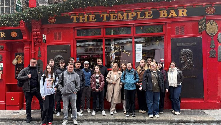 Achtzehn Personen posieren lächelnd in einer Reihe vor der roten Fassade des Pubs „The Temple Bar" in Dublin mit goldenem Schriftzug und Hausnummer 48.