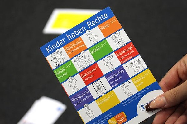 Theorie meets Praxis Eine Hand hält eine bunte Karte mit der Überschrift "Kinder haben Rechte" in der Hand. Auf der Karte sind abwechselnd die Kinder-Rechte und eine passende Skizzierung dazu abgebildet.
