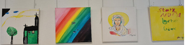 Vier Kinderbilder an einer weißen Wand, darunter eine Kirche, ein Regenbogen, ein Heiligenbild und ein gelbes Bild mit Schriftzug „stark, mutig, besser leben“.