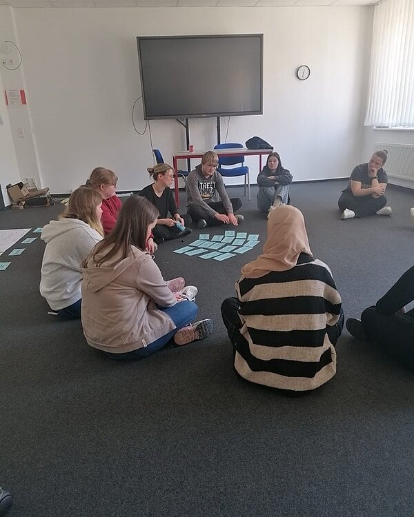 Theaterbesuch und Workshop Auszubildende sitzen zum Theaterworkshop auf dem Teppichboden und arbeiten in der Gruppe.