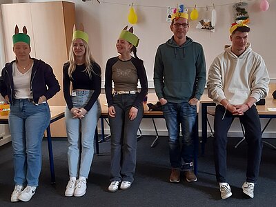 Fünf Personen stehen nebeneinander und tragen selbstgebastelte Kopfbedeckungen mit Ohren wie Osterhasen.