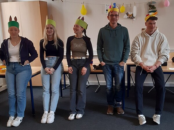 Fünf Personen stehen nebeneinander und tragen selbstgebastelte Kopfbedeckungen mit Ohren wie Osterhasen.