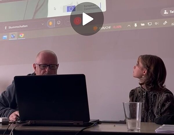 Online-Konferenz mit der EU-Kommission Teilnehmende der Online-Konferenz sitzen am Schreibtisch und Laptop, hinter ihnen werden per Beamer live weitere Teilnehmer gezeigt.