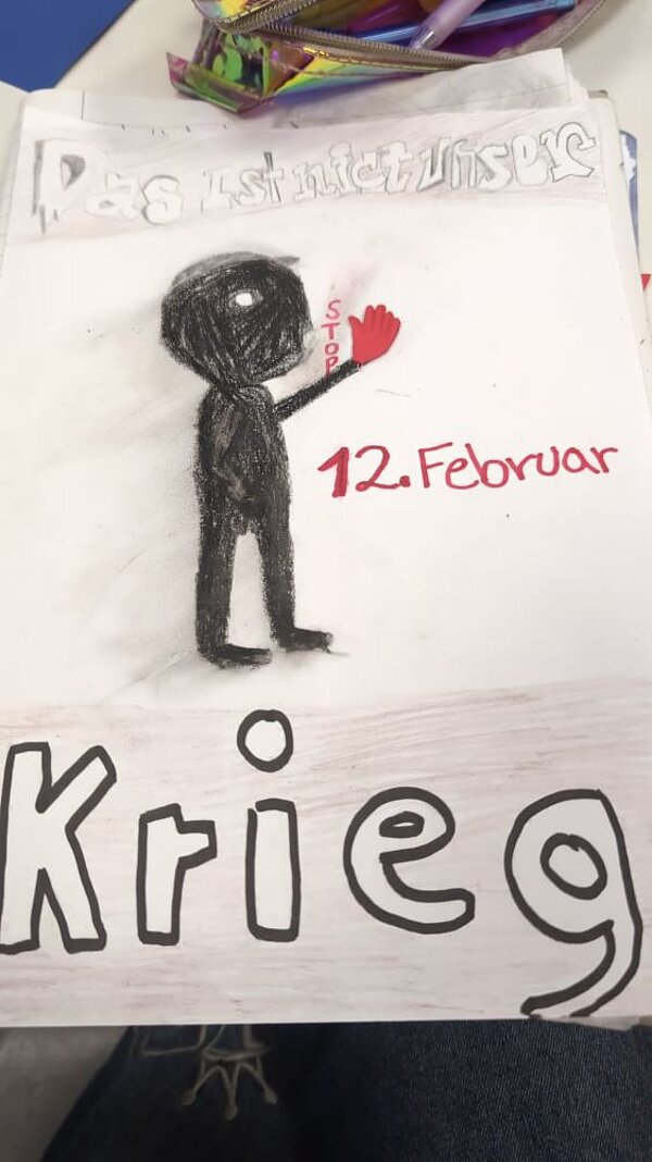 Eine Zeichnung auf weißem Papier: Eine schwarze Figur mit dem Wort "Stop" vor dem Mund und eine rote Hand hochhält. Darüber steht "Das ist nicht unser" in hellen Lettern und darunter steht ‚12. Februar‘ in roter Schrift und das Wort ‚Krieg‘ ist groß und fett geschrieben.