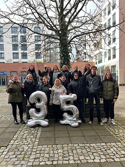 Schüler*innen posieren gemeinsam auf einem Innenhof vor silbernen Ballonzahlen „35“ und feiern das Jubiläum der Euro-Schulen und Euro Akademie.