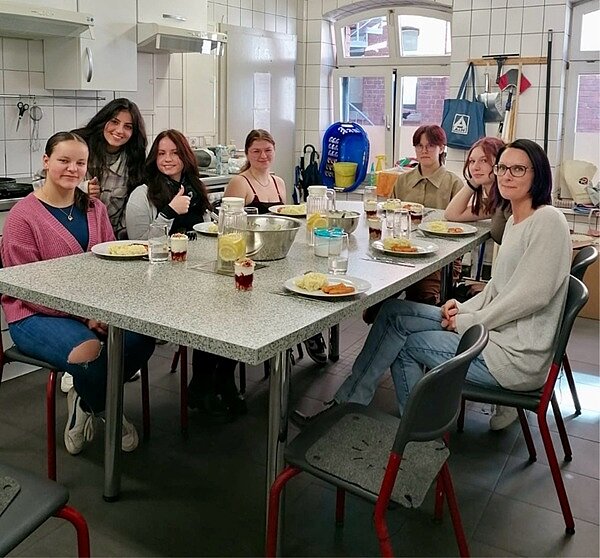 An die Töpfe, fertig, los! Die Auszubildenden sitzen gemeinsam an einem großen gedeckten Tisch und posieren für ein Foto.