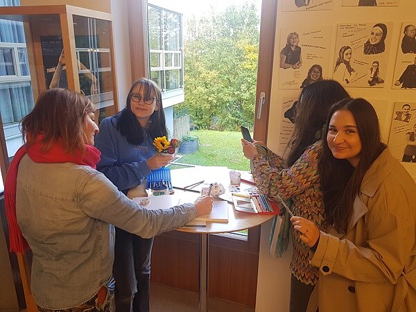 Vier weibliche Studierende an einem Stehtisch, auf dem Stifte liegen, erarbeiten etwas zum Thema Migrationspädagogik.