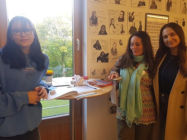 Drei weibliche Studierende posieren um den Stehtisch für ein Foto.