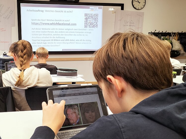 Ein Junge sitzt an einem Tisch in einem Klassenraum und schaut auf ein Tablett.