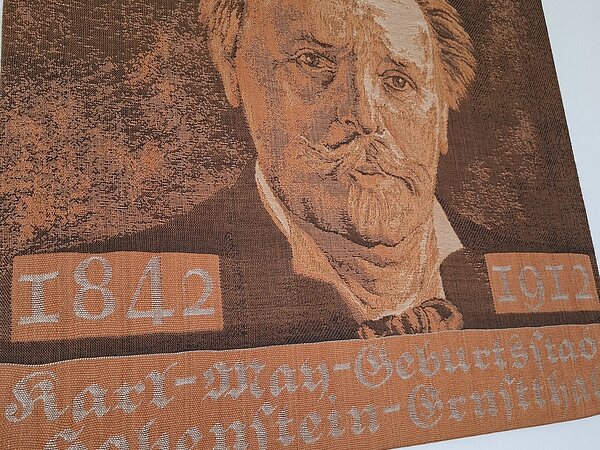 Ein Wandbild von Karl May, darunter steht 1842-1912 und "Karl-May-Geburtsstadt Hohenstein-Ernstthal".