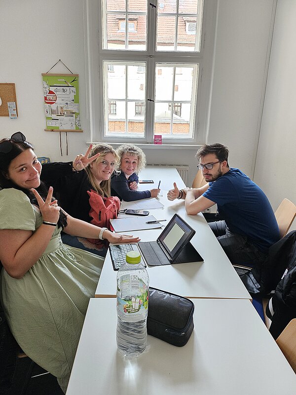 Podcast-Projekt: KAFFEE TRINKEN & SPIELEN Schülerinnen und Schüler der Euro Akademie Halle sitzen an einem langen Tisch und planen ihr Projekt, in der Mitte steht ein Tablett.
