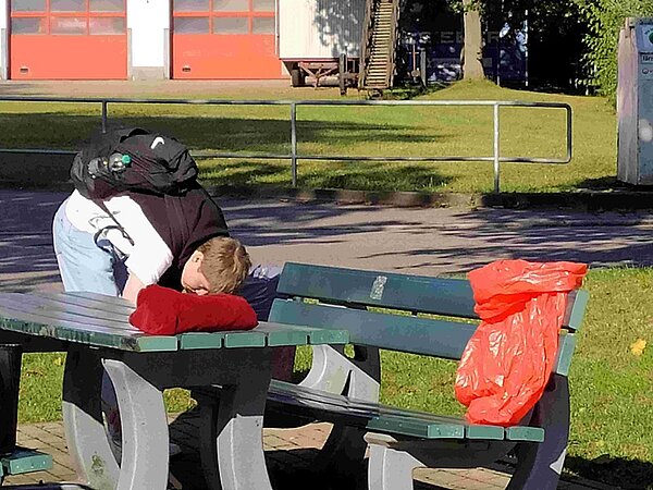 Schüler bückt sich, um Abfall unter einem öffentlichen Tisch und Parkbank aufzusammeln.