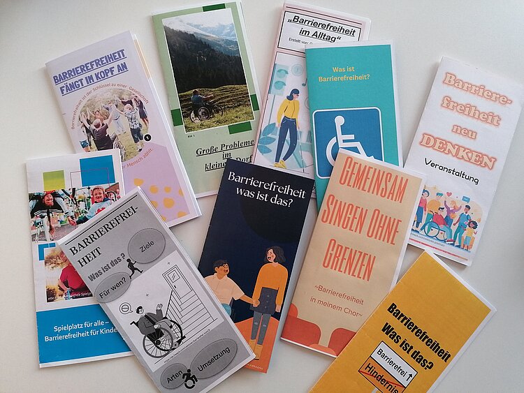 Praktikumsvorbereitungen der Sozialassistent*innen Flyer mit orangenen oder blauen Hintergrund liegen auf einer weißen Tischplatte. Inhaltlich wurden die Flyer von den Sozialassistent*innen erarbeitet und handeln von Barrierefreiheit.