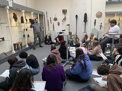 Schülerinnen und Schüler sitzen auf dem Boden und hören dem Leiter des Kunstauktionshauses zu.