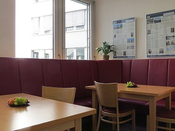 Blick in die Cafeteria der Euro Akademie Dresden, mit Sitzecke in der Farbe Burgundy, Holztischen und Stühlen.