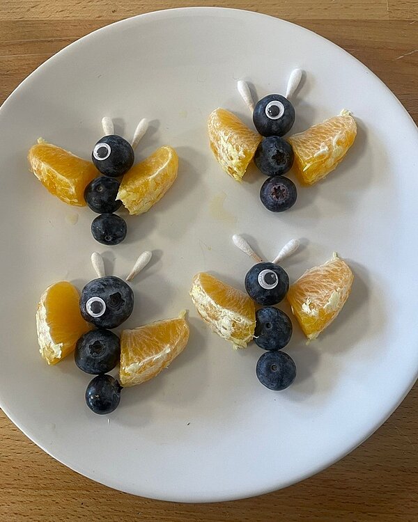 Schmetterlinge aus Blaubeeren als Körper, mit Mandarinen als Flügel und abgeschnittene Wattestäbchen als Fühler.