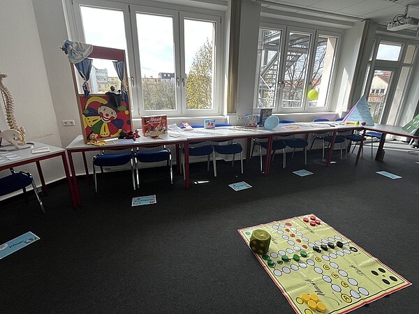 Tag der offenen Tür Im großen Klassenraum sin die Tische an die Fensterfront geschoben, auf ihnen lieben Unterrichtsmaterialien, ein Puppentheater, auf dem Boden ein großes Brettspiel.
