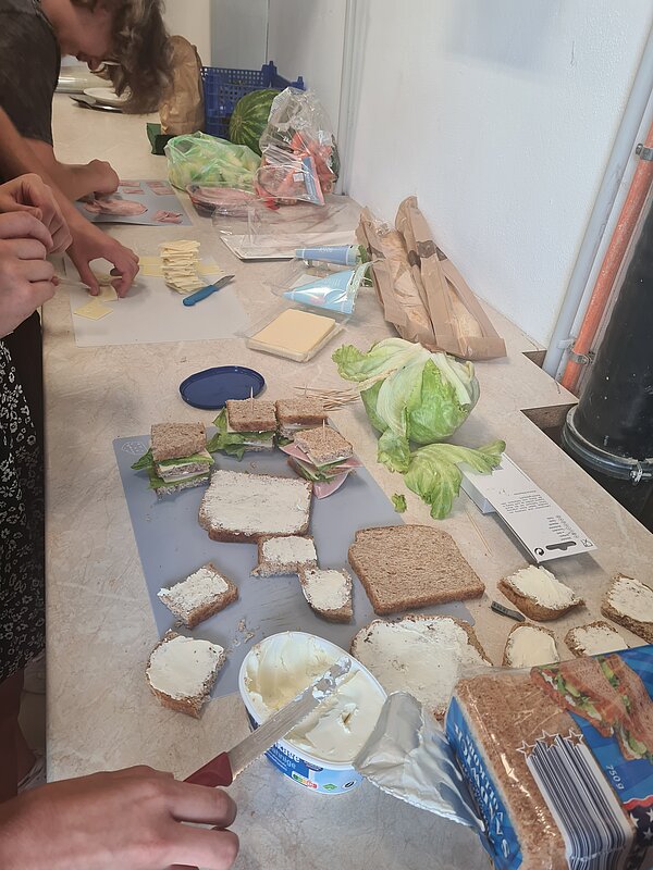 DRK Werkstätten Geithain - Aktionstag gesunde Ernährung Zu sehen ist ein langer Tisch, auf dem Brote mit Frischkäse, Quark und Käse geschmiert werden.