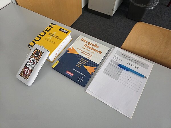 Abschlussprüfung im Fach Mathematik an der Euro Akademie Dresden Auf einem weißen Tisch liegt ein Deutsch-Duden, ein Kugelschreiber, Arbeitsblätter zut Prüfung sowie ein Lehrbuch.