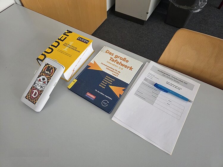 Abschlussprüfung im Fach Mathematik an der Euro Akademie Dresden Auf einem weißen Tisch liegt ein Deutsch-Duden, ein Kugelschreiber, Arbeitsblätter zut Prüfung sowie ein Lehrbuch.