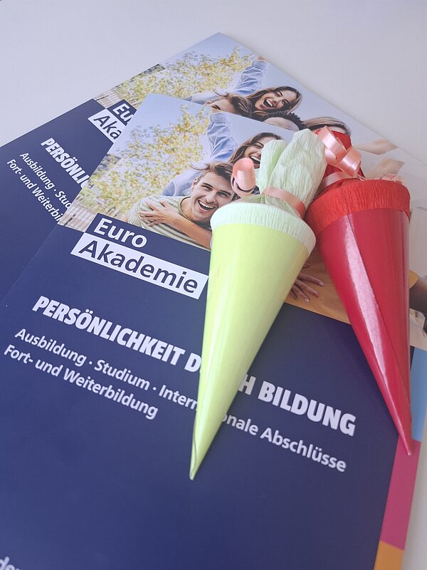 Broschüren der Euro Akademie mit Informationen zu Ausbildung, Studium sowie Fort- und Weiterbildung; darauf liegen zwei kleine bunte Schultüten.