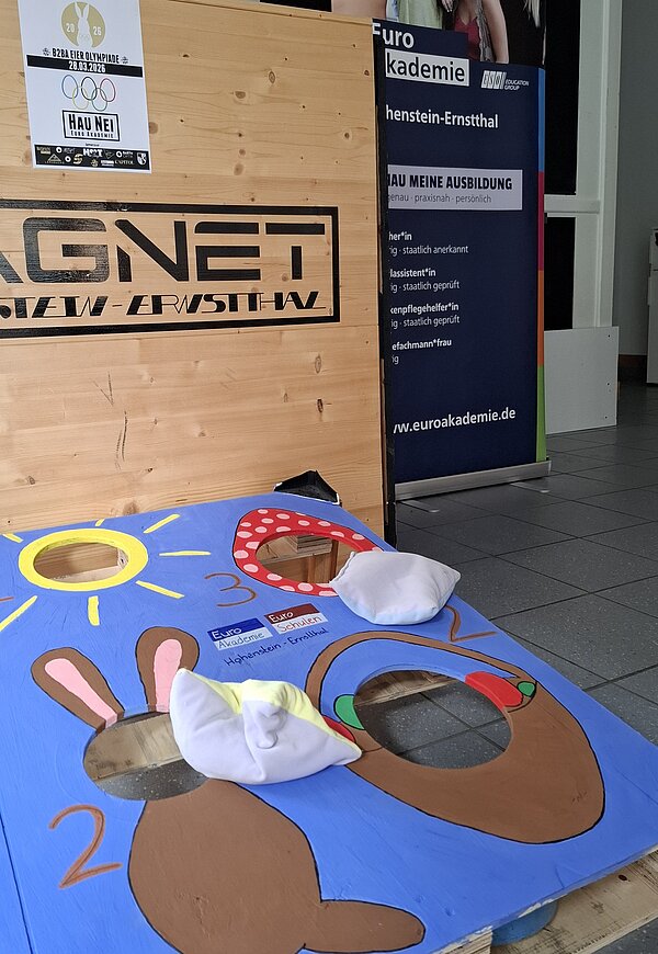 Nahaufnahme eines bunten Oster-Wurfspiels mit Hasen- und Eiermotiven vor einer Holzwand mit Magnet-Schriftzug.