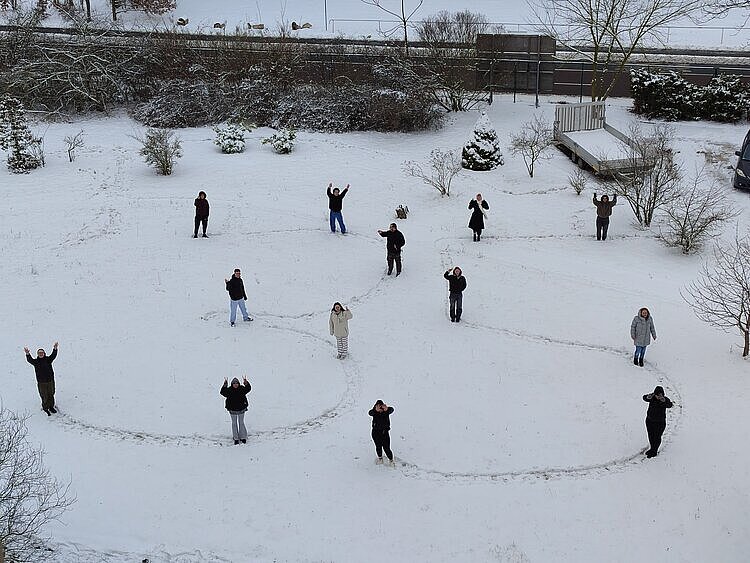 Sicht von oben auf einen schneebedeckten Platz, auf dem Schüler die Zahl 35 in den Schnee geschrieben haben; die Schüler stehen dabei und winken.
