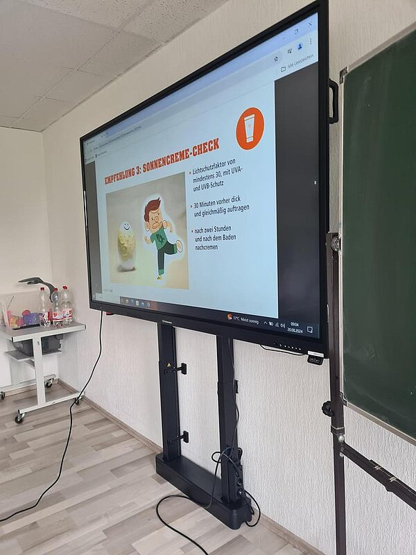 Auszeichnung „Clever in Sonne und Schatten“ 2024 Auf dem Bildschirm wird ein Teil einer Präsentation angezeigt: "Empfehlung 3: Sonnencreme-Check"