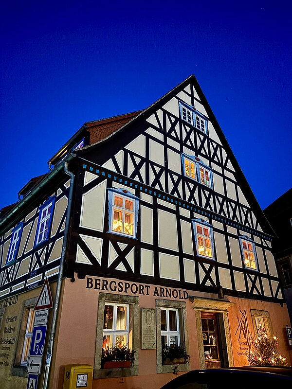 Beleuchtetes Fachwerkhaus bei Nacht mit der Aufschrift „Bergsport Arnold“, warme Fensterlichter vor tiefblauem Abendhimmel.