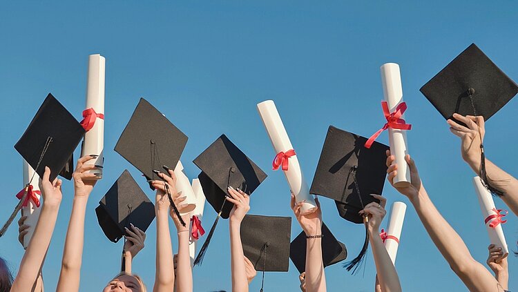 Glückliche Absolventen, die ihre Abschlusszeugnisse und Diplome in die Luft werfen.