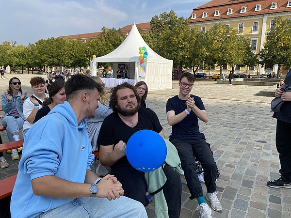 Landestag 2024 Zwei junge Männer sitzen auf einer Festzeltgarnitur und der rechte Mann hält einen blauen Ballon in der Hand.