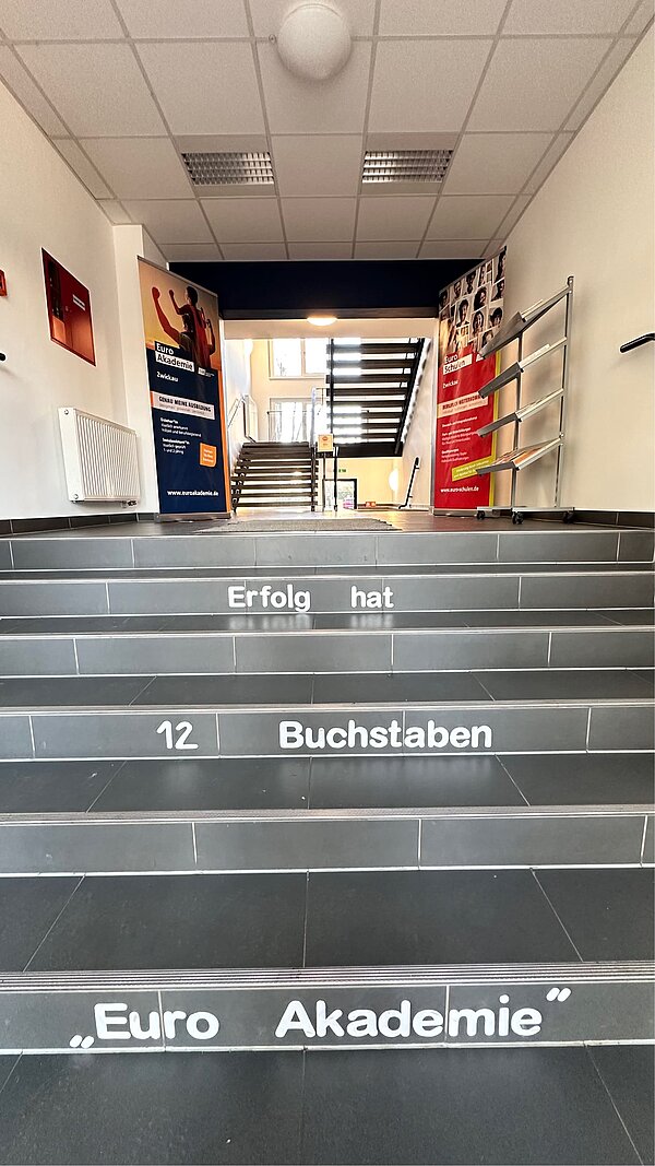 Aus Rot wird Blau: Malerarbeiten abschlossen Eine grau geflieste Treppe, auf deren Stufen steht: "Erfolg hat 12 Buchstaben: Euro Akademie