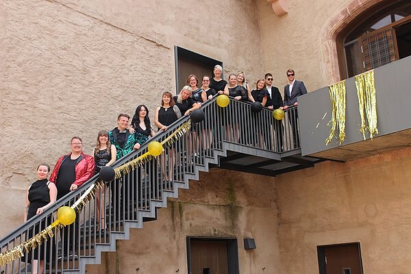 Ein Tag voller Glanz, Emotionen und unvergesslicher Erinnerungen Absolventinnen und Absolventen posieren auf einer langen Treppe des Schlosses in Rochlitz hintereinanderstehend am Geländer für ein Gruppenfoto.
