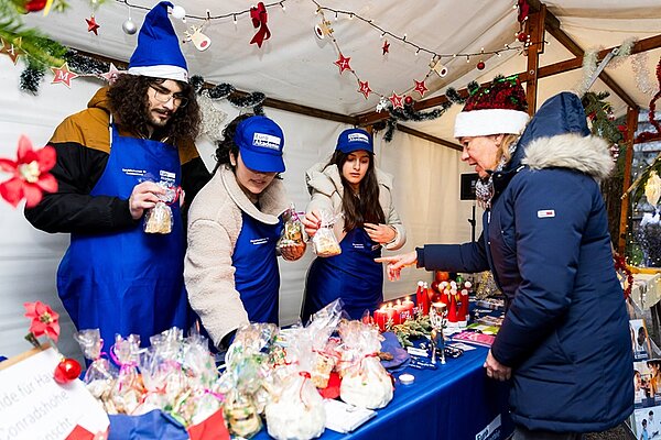 Euro Akademie Berlin begeistert beim Wintermarkt Schülerinnen und Schüler stehen an ihrem schön angerichteten Wintermarkt-Stand und verkaufen Plätzchen und Kuchen.