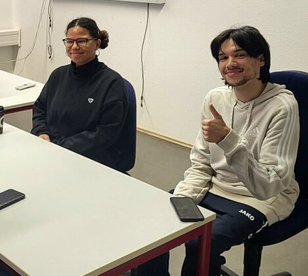 Drei Auszubildende der Euro Akademie Hannover sitzen gemeinsam an einem weißen Tisch und posieren lächelnd für ein Foto.