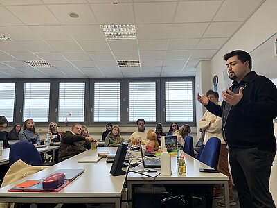 Man sieht Niklas Wagener von der Seite, wie er gestikulierend eine Frage der Schülerschaft beantwortet. Die Schüler*innen hören gespannt zu und richten ihre Augen auf den Bundestagsabgeordneten.