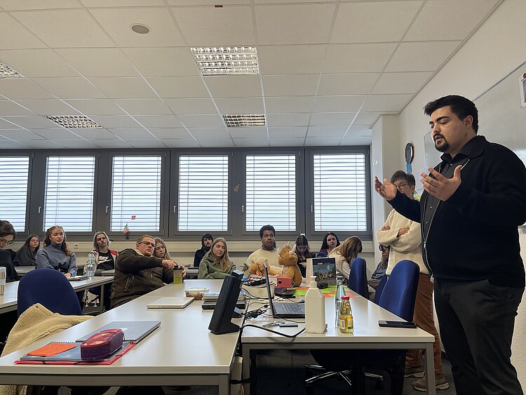 Besuch eines Bundestagsabgeordneten: Niklas Wagener an der Euro Akademie Man sieht Niklas Wagener von der Seite, wie er gestikulierend eine Frage der Schülerschaft beantwortet. Die Schüler*innen hören gespannt zu und richten ihre Augen auf den Bundestagsabgeordneten.